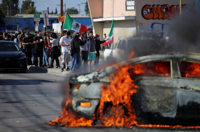 Manifestantes perto de um carro em chamas ap&oacute;s v&aacute;rias deten&ccedil;&otilde;es pelo Servi&ccedil;o de Imigra&ccedil;&atilde;o e Alf&acirc;ndega (ICE)