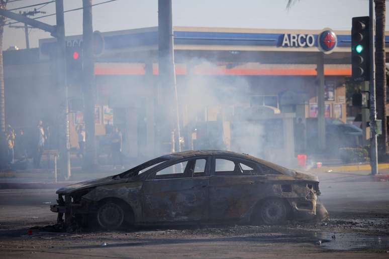 Carro destru&iacute;do na estrada durante confronto entre a pol&iacute;cia e manifestantes ap&oacute;s deten&ccedil;&otilde;es pelo Servi&ccedil;o de Imigra&ccedil;&atilde;o e Alf&acirc;ndega (ICE), na cidade de Paramount, no Condado de Los Angeles, em 7 de junho