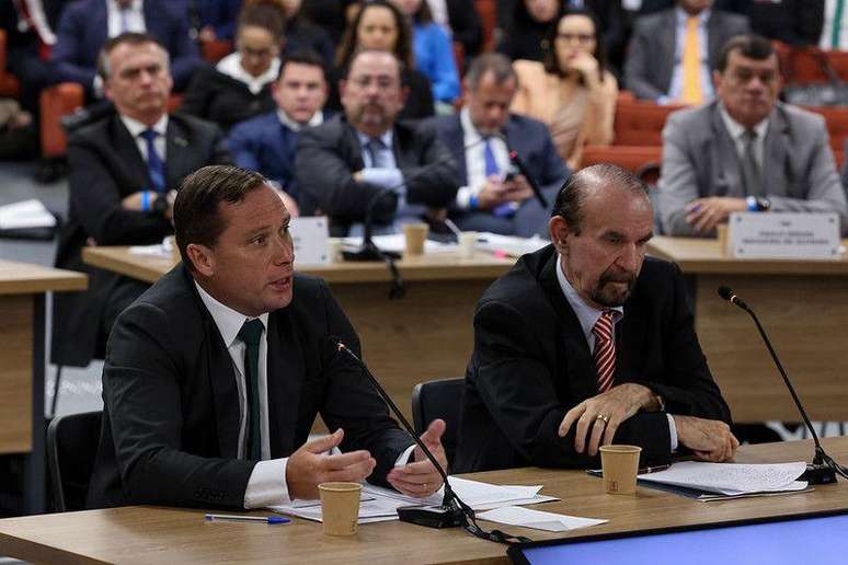 Mauro Cid ao microfone com Jair Bolsonaro ao fundo