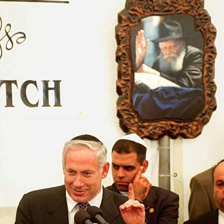 Em foto de 1996, quando era primeiro-ministro de Israel tal como atualmente, Benjamin Netanyahu aponta para foto do rabino Menachem Mendel Schneerson ap&oacute;s visitar o t&uacute;mulo do l&iacute;der religioso em Nova York