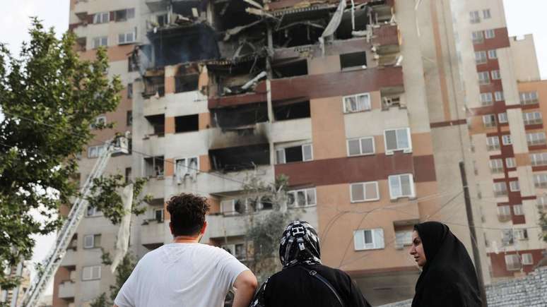 Pessoas observam um prédio danificado após ataques israelenses em Teerã, no Irã
