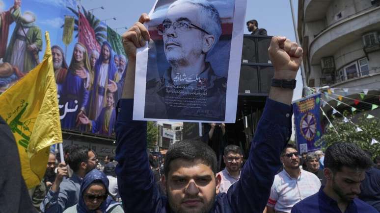 Manifestante iraniano segura cartaz do Chefe do Estado-Maior das Forças Armadas, Mohammad Bagheri, que foi morto em um ataque israelense, durante uma manifestação contra Israel em Teerã.