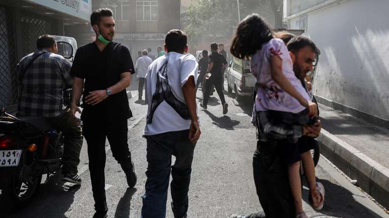 Pessoas correm por uma rua em meio à fumaça após os ataques israelenses a Teerã, capital do Irã