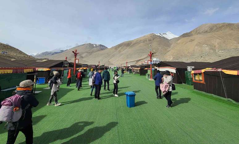 Turistas caminhando em uma passarela de astroturf verde no acampamento base norte do Everest.