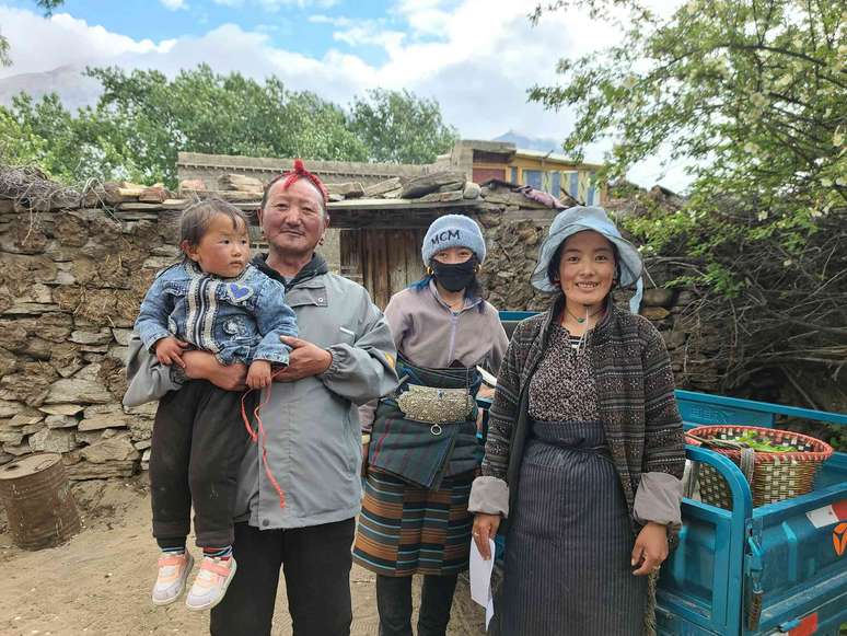 Uma família tibetana em frente à sua fazenda, incluindo um homem segurando uma criança pequena.