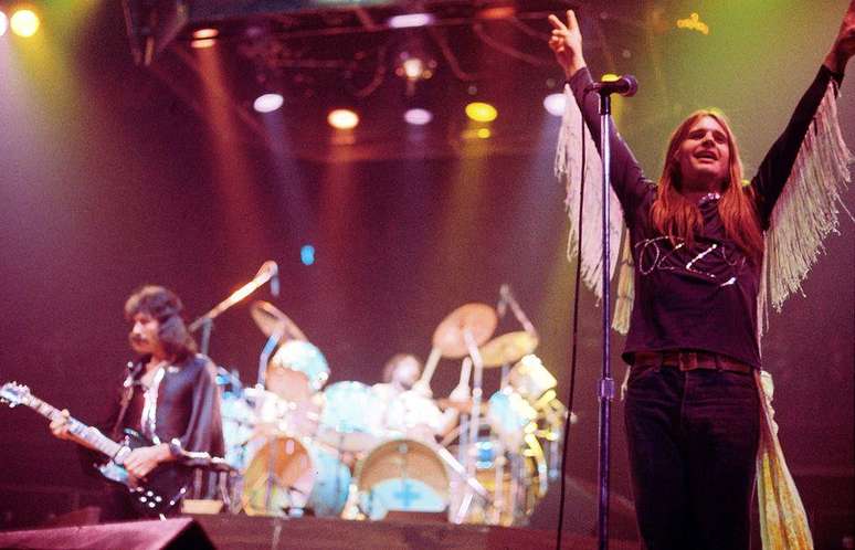 Ozzy Osbourne com os bra&ccedil;os no ar no palco com Tony Iommi em 1976