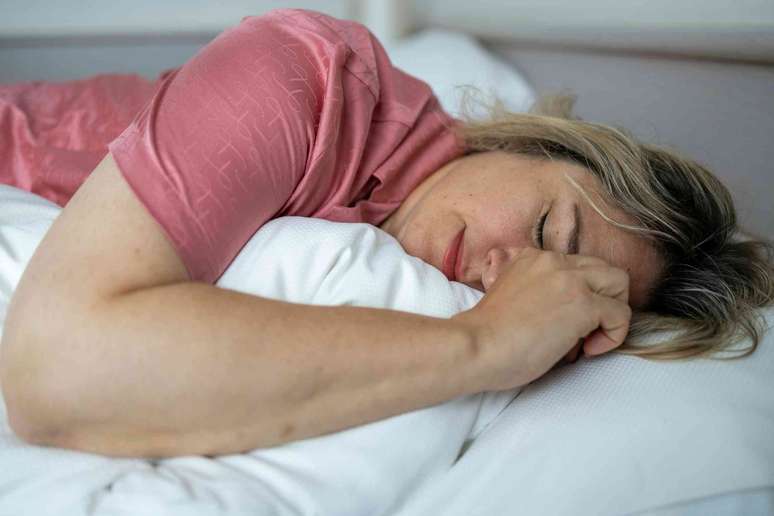 Person who lies laterally on the bed, the eyes closed, possibly making a grimace
