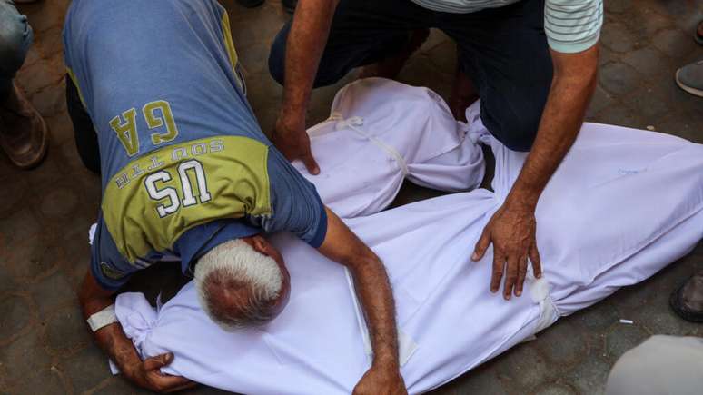 Moradores palestinos choram sobre os corpos de seus familiares mortos durante ataque israelense visando a escola Mustafa Hafez, em Gaza, em 3 de julho de 2025.