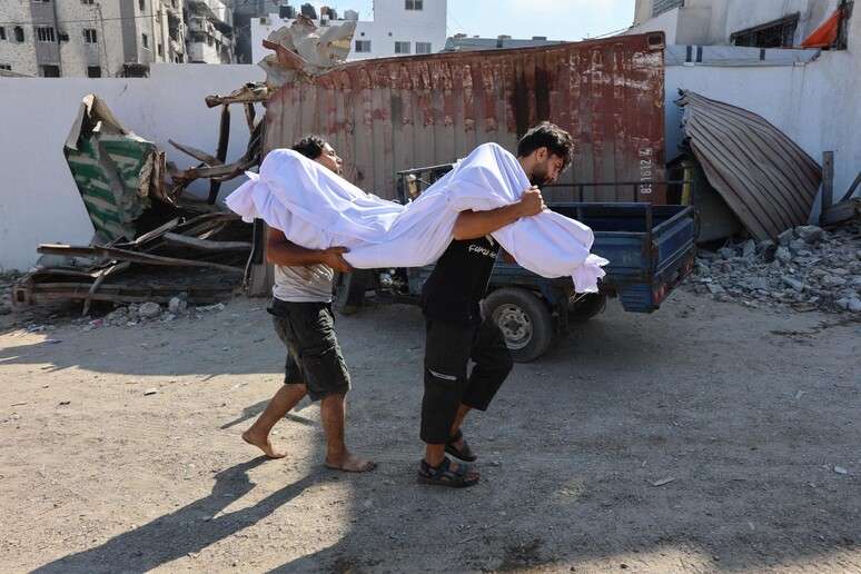 Palestinos carregam corpo de vítima em ataques de áreas humanitárias