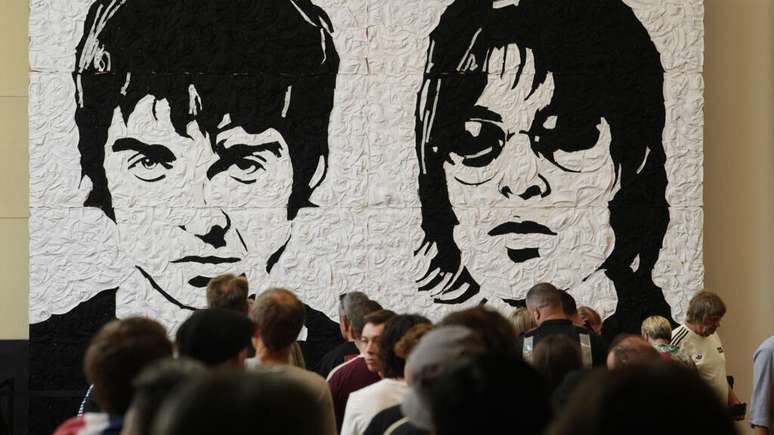 Às vésperas do primeiro show da aguardada turnê de reunião do Oasis, fãs tiram fotos em frente ao “Wonder Wall”, um mural criado pelo artista galês Nathan Wyburn no shopping St David’s, em Cardiff. O mural virou ponto de encontro e celebração para os admiradores do grupo britânico, que abre sua turnê global nesta sexta-feira, 4 de julho de 2025, com casa cheia no Principality Stadium, no País de Gales.