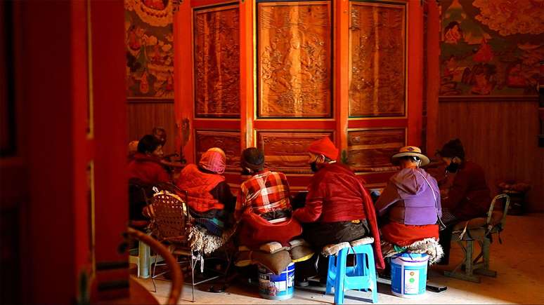 Mulheres tibetanas sentadas em volta de uma roda de oração em monastério