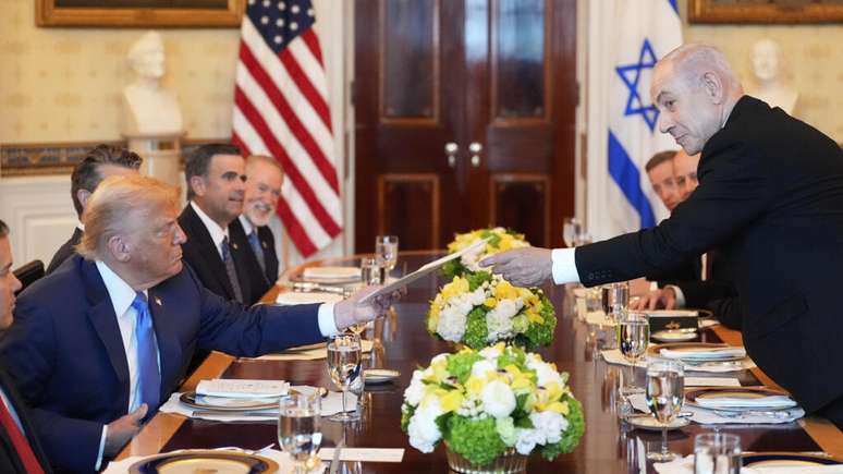 O primeiro-ministro de Israel, Benjamin Netanyahu, à direita, entrega uma pasta ao presidente Donald Trump durante uma reunião no Salão Azul da Casa Branca. 7 de julho de 2025