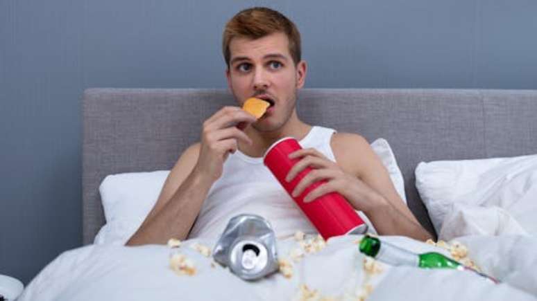 A man is eating snacks in a dirty bed. Andrey_Popov/Shutterstock