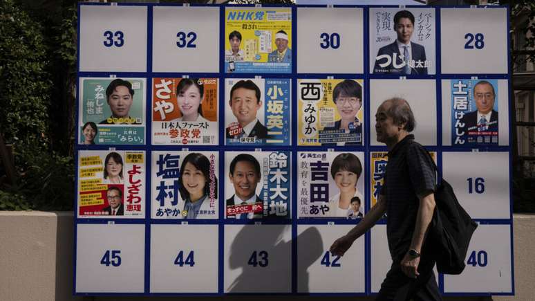 Pedestre passa diante de painel eleitoral com candidatos para a eleição para a Câmara Alta, no próximo domingo (20). Tóquio, 18/07/25.