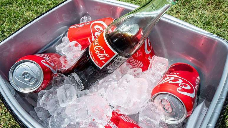 Um cooler com gelo cheio de latas e uma garrafa de Coca-Cola