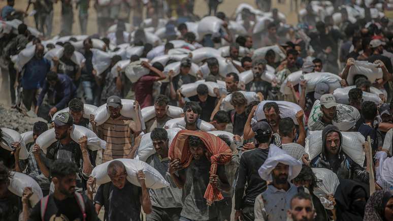 Palestinos deslocados internamente tentam pegar sacos de farinha de um caminh&atilde;o de ajuda pr&oacute;ximo a um ponto de distribui&ccedil;&atilde;o de alimentos em Zikim, no norte da Faixa de Gaza, em 27 de julho de 2025