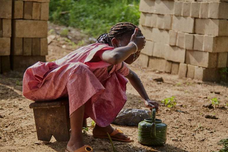 Antes de um ritual de oração, criança lava o rosto na Costa do Marfim. Família de seis mulheres veio de Burkina Faso.