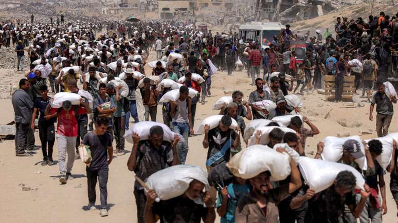 Palestinos caminham com sacos de farinha depois que caminhões carregados de ajuda humanitária entraram no norte de Gaza, em 27 de julho de 2025.