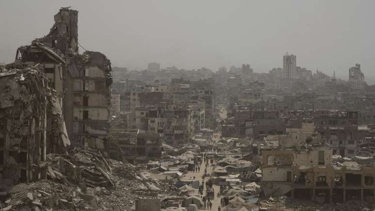 Pessoas caminham por uma rua ladeada por prédios destruídos após bombardeios israelenses durante a guerra entre Israel e o Hamas na Faixa de Gaza, terça-feira, 29 de julho de 2025.