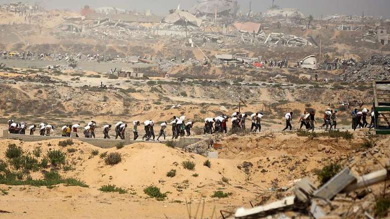 Palestinos carregam sacos de farinha de caminh&otilde;es de ajuda humanit&aacute;ria que chegam do cruzamento de fronteira em Zikim, no norte da Faixa de Gaza