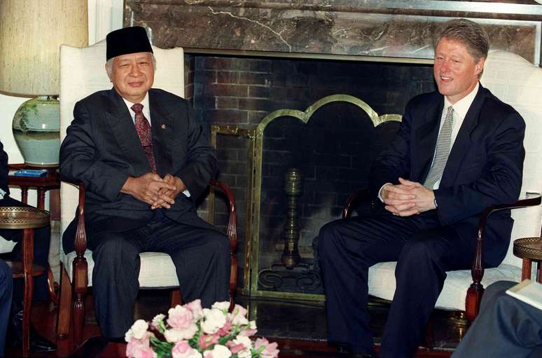 Dois homens sentados em cadeiras de espaldar alto em frente a uma lareira.