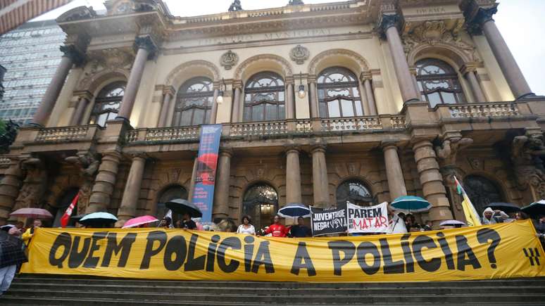 Manifesta&ccedil;&atilde;o em frente ao Theatro Municipal em S&atilde;o Paulo contra a viol&ecirc;ncia policial exibe uma grande faixa amarela com os dizeres "quem policia a pol&iacute;cia?" em preto.