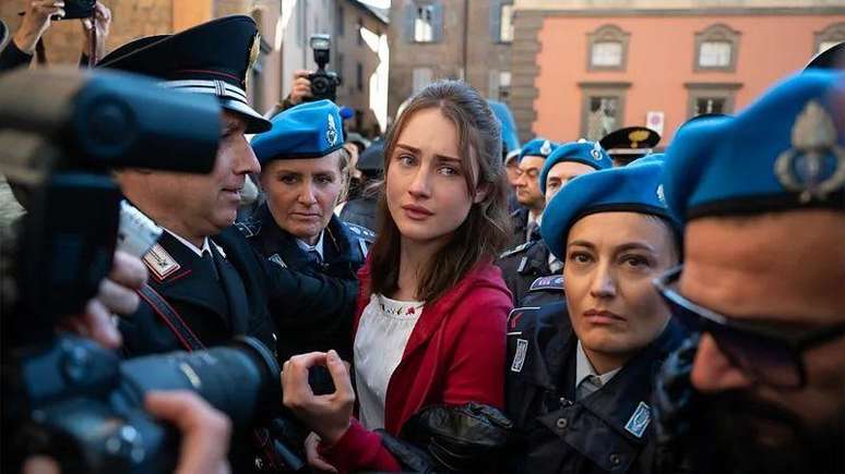 A atriz Grace Van Patten, no papel de Amanda Knox, avan&ccedil;a por um grupo de jornalistas que tentam fotograf&aacute;-la, enquanto &eacute; protegida por v&aacute;rios policiais