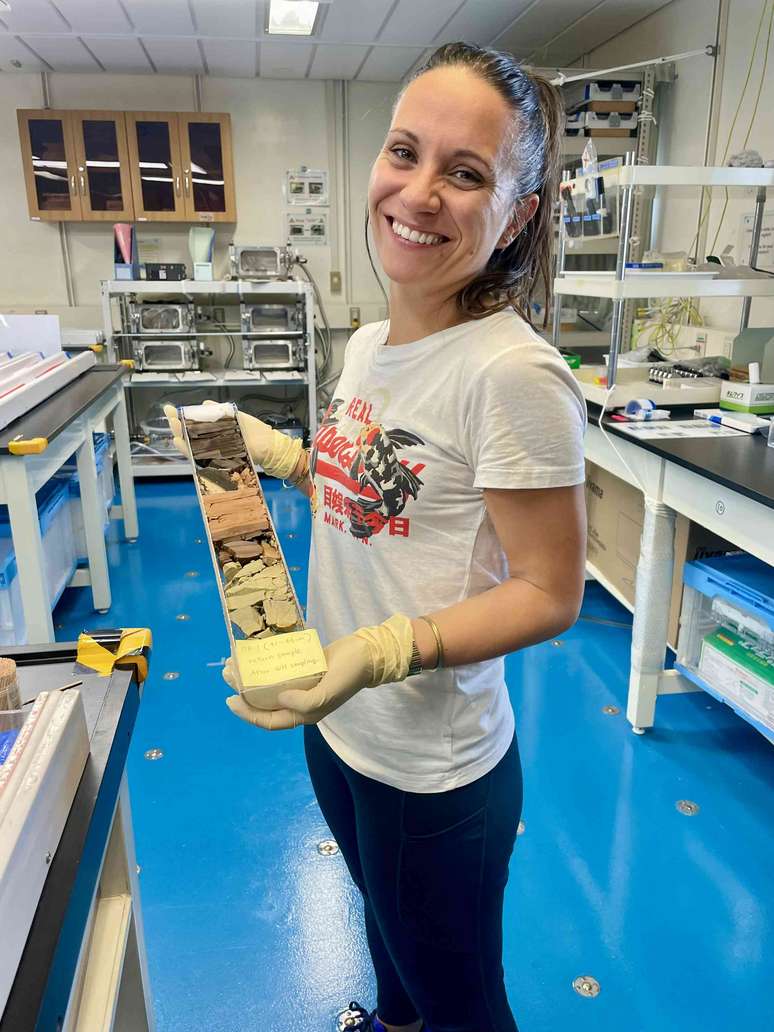 uma mulher segurando um tubo cheio de camadas de sedimentos de cores diferentes