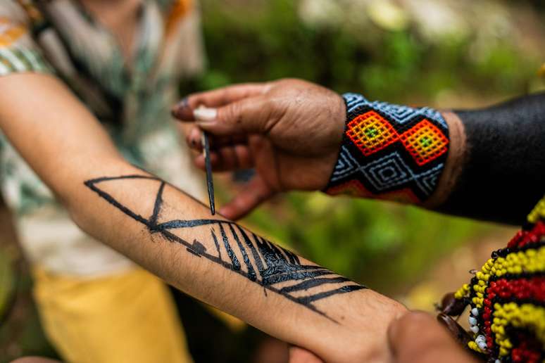 Turista fazendo pintura ind&iacute;gena tradicional com Jenipapo durante turn&ecirc; em tribo brasileira