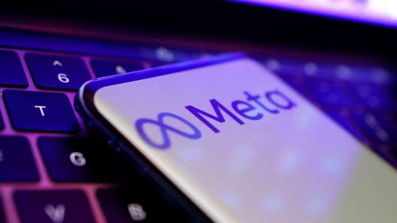 Um telefone posicionado sobre um teclado de laptop. O telefone exibe o logotipo do Meta com o símbolo do infinito e a palavra 