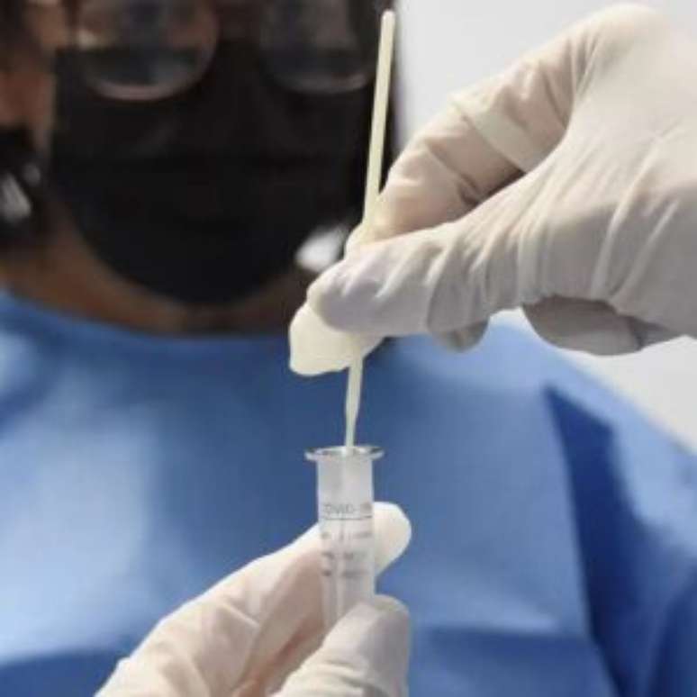 Cientistas com frasco para analisar Covid-19.