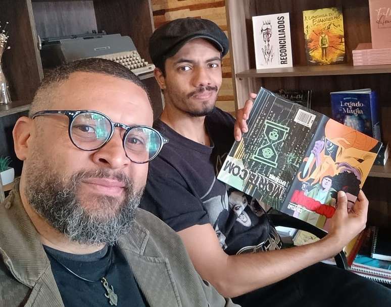 Cassiano Nascimento e Isaque Sagara, que segura HQ aberta, mostrando as duas capas do mesmo volume.