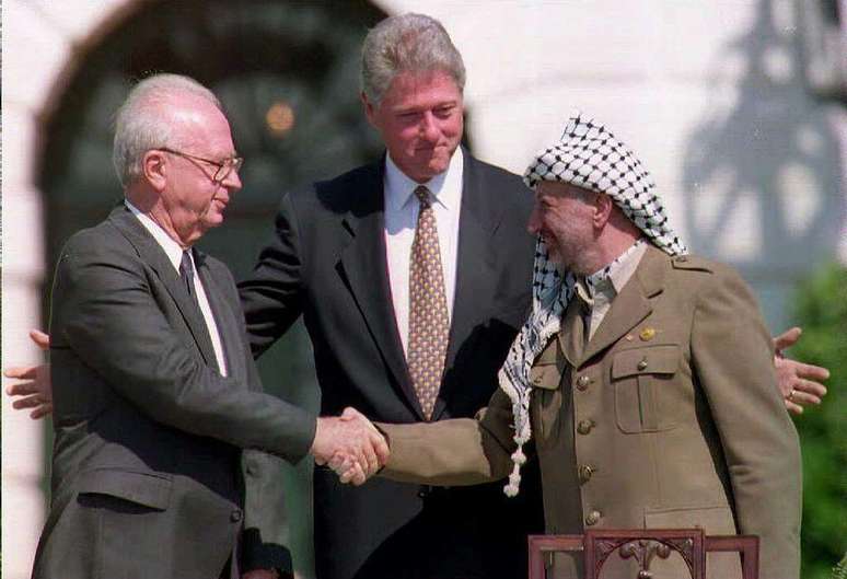 Esta foto de arquivo de 13 de setembro de 1993 mostra o presidente dos EUA, Bill Clinton (centro), entre o l&iacute;der da OLP, Yasser Arafat (direita), enquanto ele aperta a m&atilde;o do primeiro-ministro israelense, Yitzahk Rabin. Rabin e Arafat apertaram as m&atilde;os pela primeira vez depois que Israel e a OLP assinaram um acordo hist&oacute;rico sobre a autonomia palestina nos territ&oacute;rios ocupados.