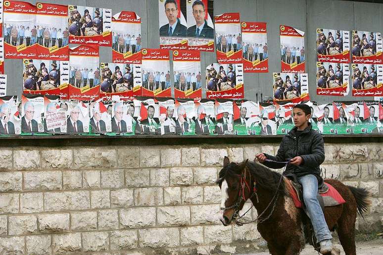 Cartazes da campanha do candidato presidencial palestino Mustafa Barghouti dominam as duas fileiras superiores de um quadro de avisos em 7 de janeiro de 2005, na cidade de Ramallah, na Cisjord&acirc;nia