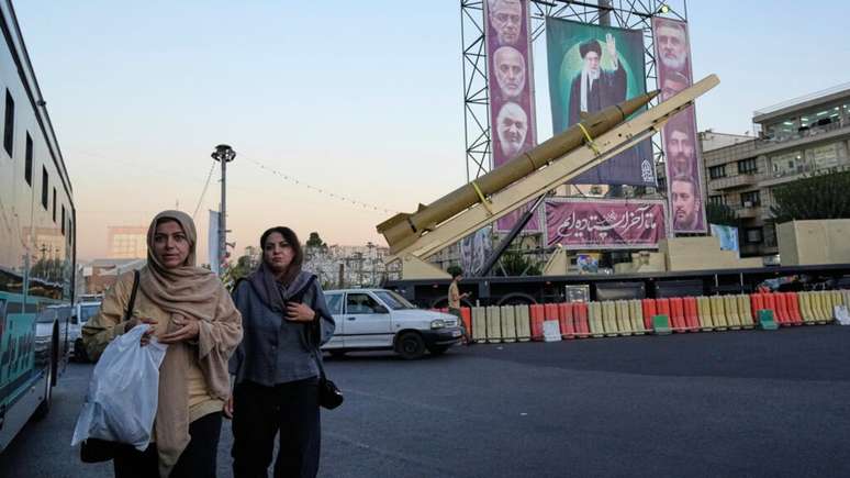 Iranianas passam diante de um míssil e de um outdoor exibindo retratos do líder supremo iraniano, o aiatolá Ali Khamenei (centro), e de militares mortos em um ataque israelense em junho. Teerã, 25 de setembro de 2025. Iranianas passam diante de um míssil e de um outdoor exibindo retratos do líder supremo iraniano, o aiatolá Ali Khamenei (centro), e de militares mortos em um ataque israelense em junho. Teerã, 25 de setembro de 2025.