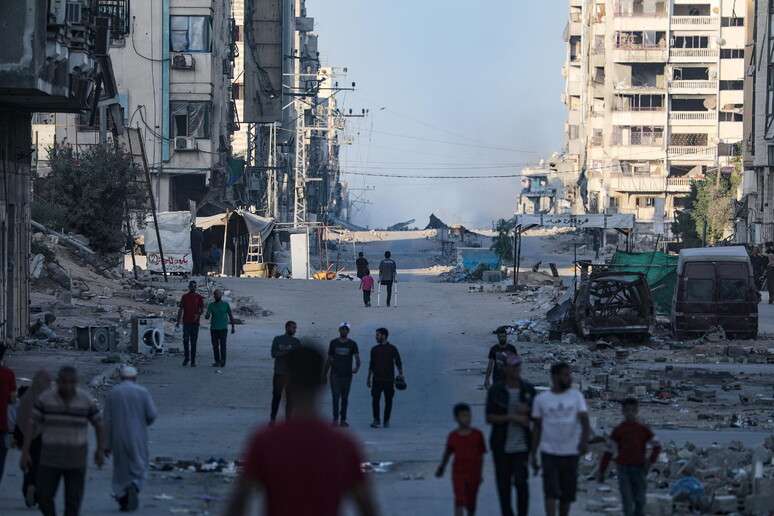 Palestinos caminham por rua devastada na Cidade de Gaza, alvo de operação militar israelense