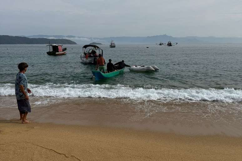 Pessoas na praia após o resgate de dupla que estava em lancha naufragada