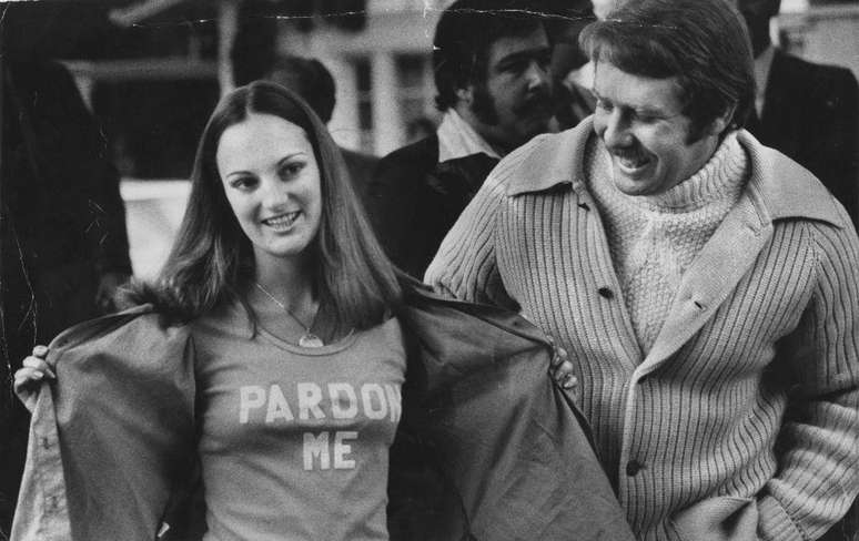 Patricia Hearst mostra uma camiseta com os dizeres "Perdoe-me" enquanto seu marido Bernard Shaw sorri ao lado dela, em 1979