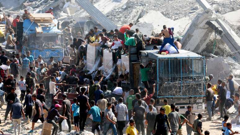 Palestinos recolhem alimentos em caminhões que entraram em Gaza, em Khan Younès, no sul da Faixa de Gaza, em 12 de outubro de 2025