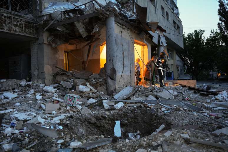 Uma idosa caminha com a ajuda de um socorrista em meio aos escombros de um prédio residencial danificado após um ataque de drone russo em 12 de junho de 2025 em Kharkiv, Ucrânia.