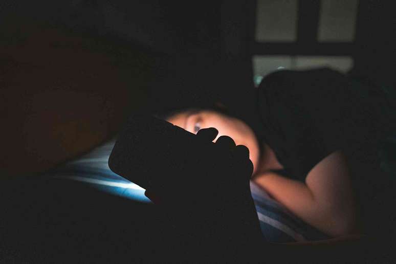 Uma mulher olhando para o celular enquanto est&aacute; deitada no escuro.