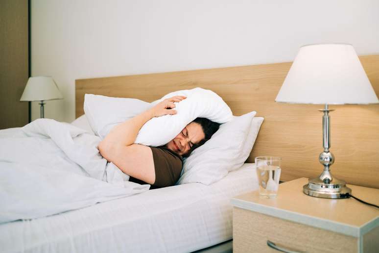 Woman lying in bed with a pillow over her head. Woman lying in bed with a pillow over her head.