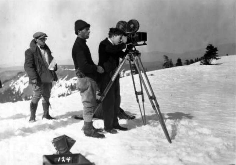 Charlie Chaplin operando uma c&acirc;mera em Em Busca do Ouro enquanto outros membros da equipe est&atilde;o pr&oacute;ximos a ele &ndash; Wikimedia Commons/Charles Chaplin Productions