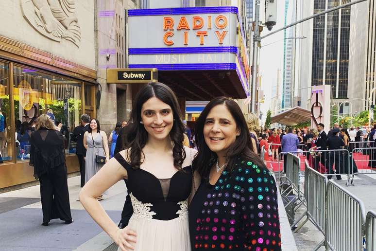 Cannold, ao lado da m&atilde;e, posa no Radio City Music Hall, em Nova York, durante o pr&ecirc;mio Tony. Ela usa um vestido branco e preto; a m&atilde;e veste um casaco