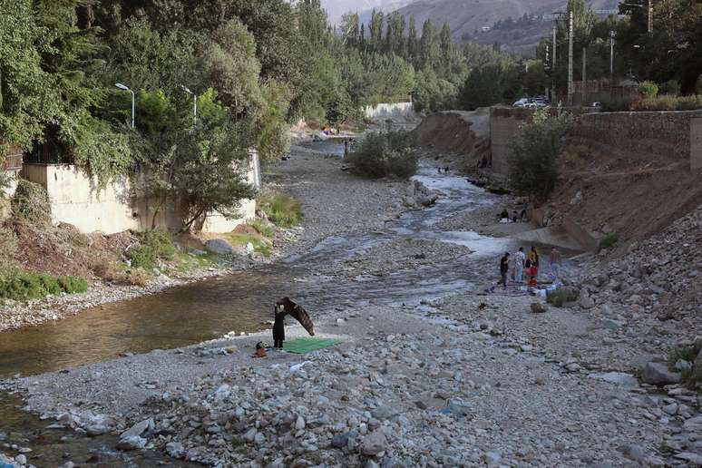 Iranianos passeiam pelo leito seco de um rio em Fasham, colocando uma esteira sobre as pedras