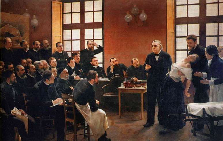 Une leçon clinique à la Salpêtrière (1887), de André Brouillet. Na tela aparece o neurologista Jean-Martin Charcot, rodeado por alunos (não havia alunas) e médicos (também não havia médicas), enquanto realiza demonstrações de hipnose em uma paciente diagnosticada com histeria. Ela, desmaiada nos braços de um assistente, é o centro da cena como objeto de observação, cujo sofrimento é transformado em espetáculo científico. Seu corpo é exposto sem consentimento, vulnerável, diante de uma multidão masculina que a observa, analisa e julga. Um reflexo da construção cultural que patologizava comportamentos femininos que escapavam à norma patriarcal na medicina do século XIX. Wikimedia Commons