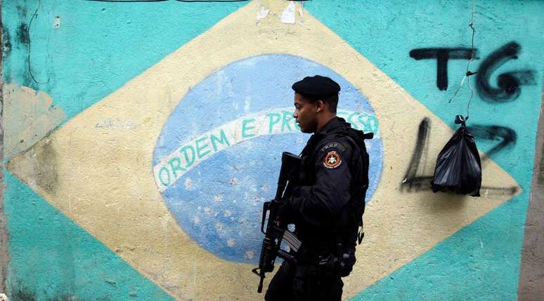 Policial passa na frente de bandeira do Brasil pintada em muro durante operação policial no Rio