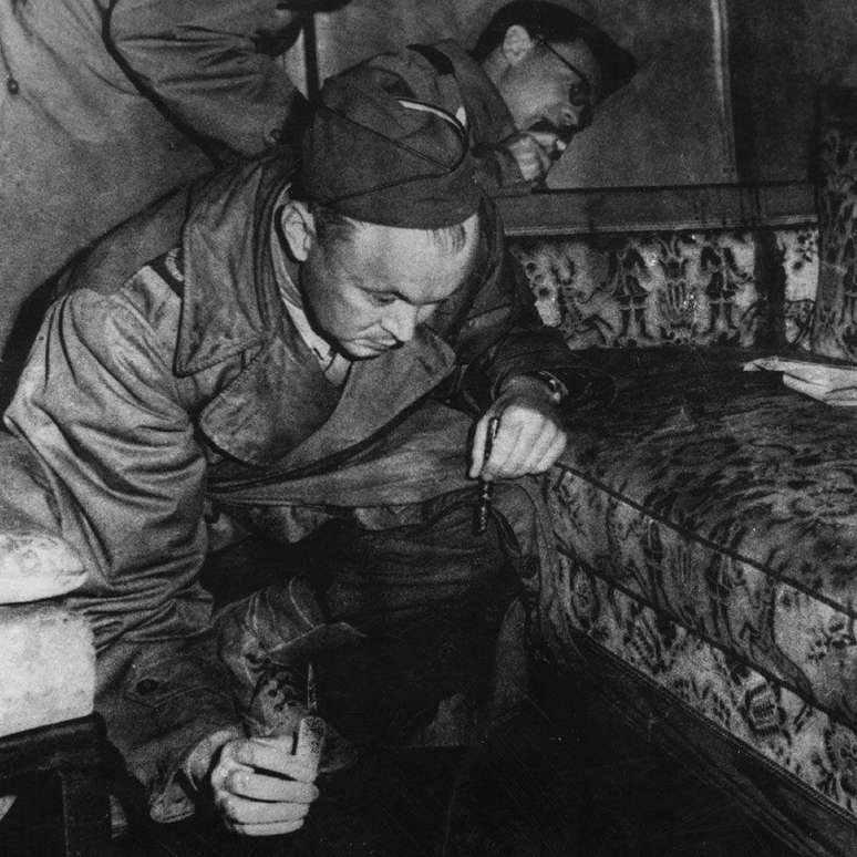 Jornalistas de guerra examinam o sof&aacute; dentro do bunker de Hitler em 1945 &mdash; acredita-se que a mancha no bra&ccedil;o da cadeira &eacute; sangue