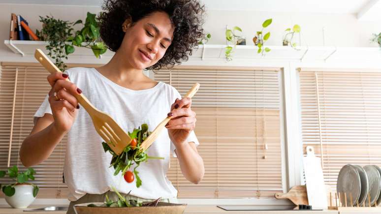 Mulher preparando salada em uma cozinha moderna, usando utens&iacute;lios de madeira para misturar verduras e tomates em uma grande tigela