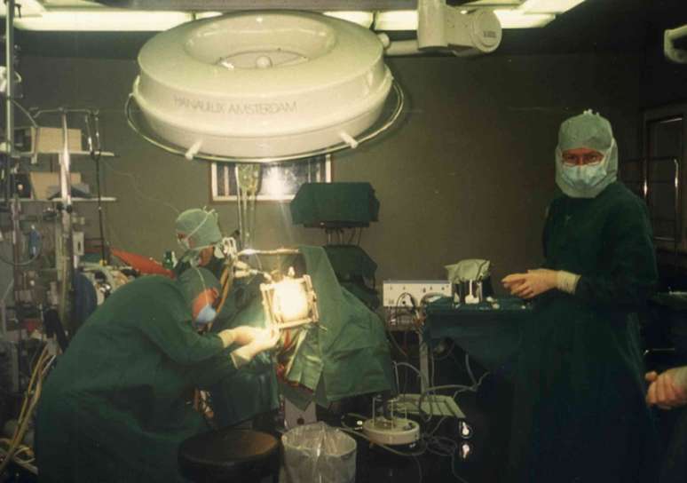 Médicos e enfermeiros vestidos com batas e máscaras preparam um paciente na sala de cirurgia.